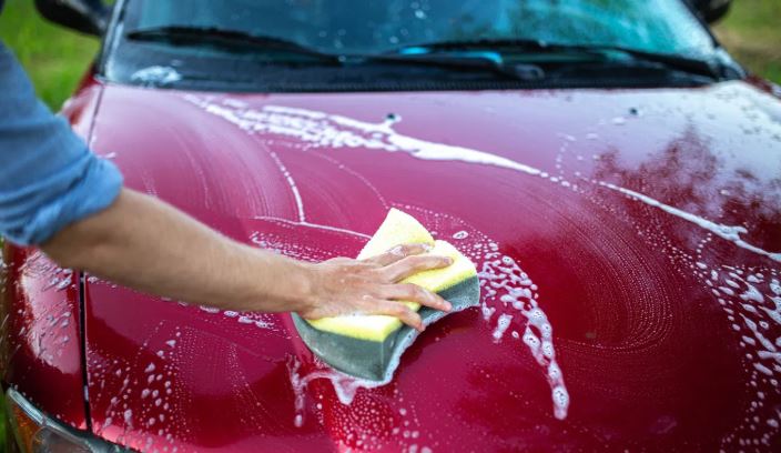 Washing a car hood with a sponge to remove dirt and residue.